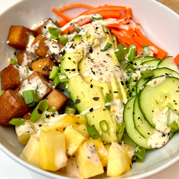 a poke bowl filled with tofu, pineapple, carrot, avocado, cucummber nd topped with kove spice
