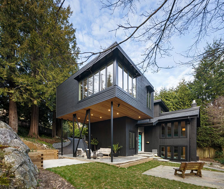 The exterior of a modern, dark wood slated home with a second level that looks like it's on stilts
