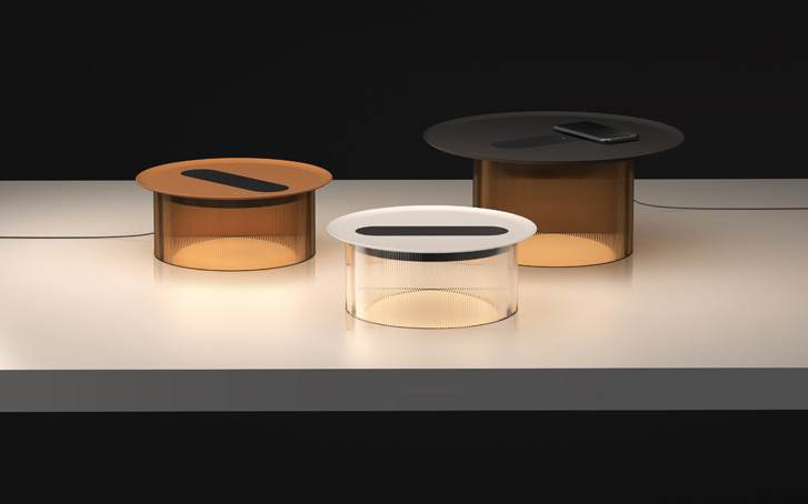 Three cylinder table-like lamps that are glowing with a LED strip on the top on a top-down lit white counter