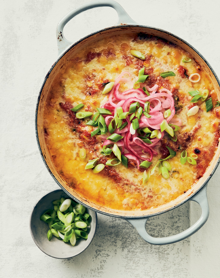 big dutch oven filled with cheesy dish topped with pickled red onions