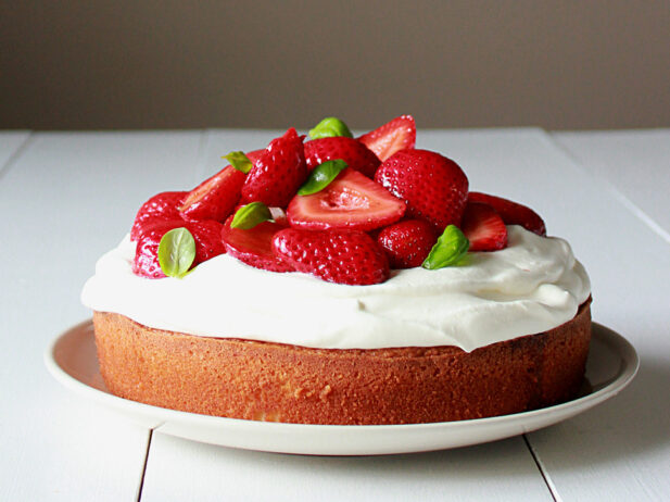Strawberries and cream topping on a round sponge cake on a plate.