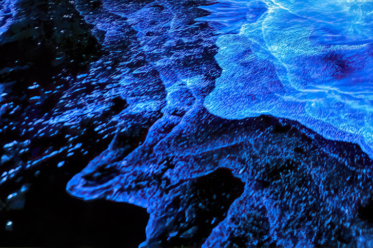 Neon white waves in fluorescent blue water at night.