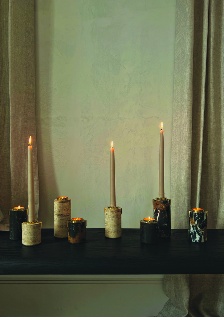 Lit white long-stemmed candles in cylinder candle holders in front of a veiled window.