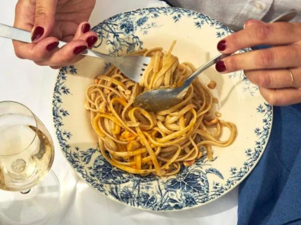 Close up pasta on ornate dish wish hands holding utensils