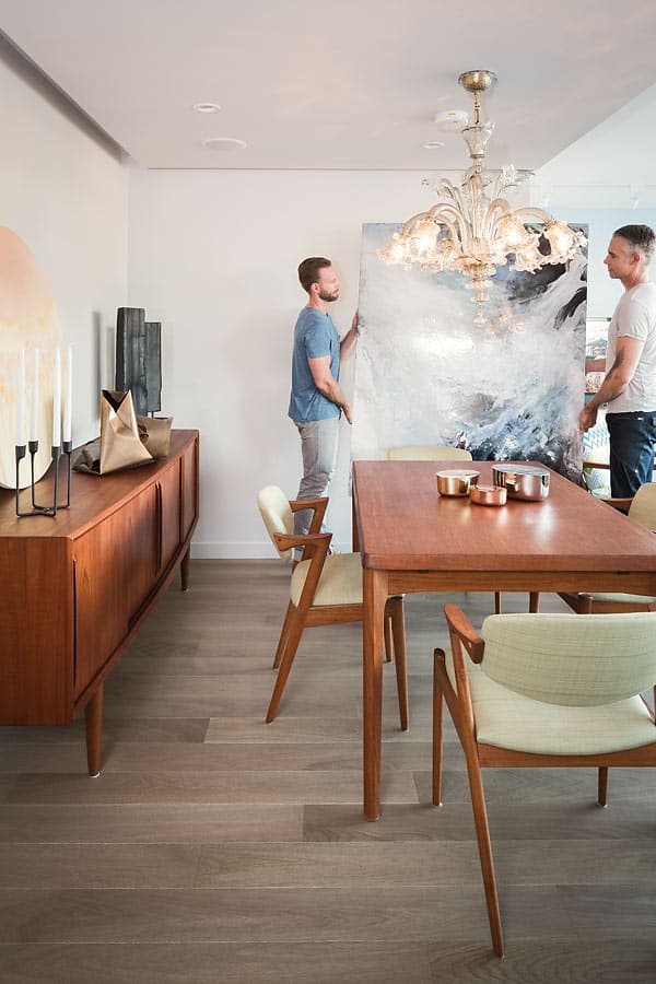 “We used large paintings with hits of colour to play off the other finishes,” says designer Chad Falkenberg (pictured left, with partner Kelly Reynolds). The pair move a piece by Vancouver painter Norah Borden into place. The round painting on the sideboard is by local artist Zoe Pawlak.