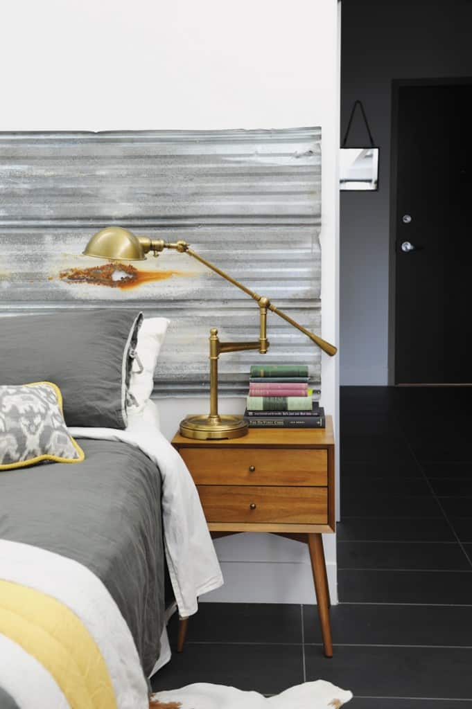 The bed is flanked with mismatched nightstands and table lamps from West Elm, but the bedroom isn't entirely devoid of coordination: the grey and yellow linens nod to the hues in the salvaged corrugated tin headboard. 