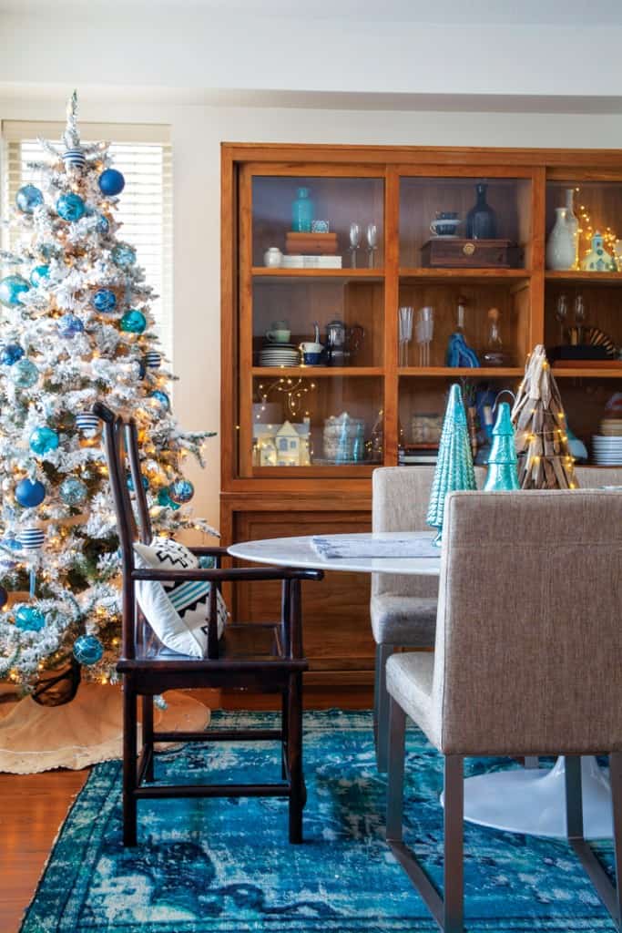 A mod Saarinen dining table is paired with a vintage hutch in the dining room; the vivid blue area rug is the jumping-off point for the blue and silver holiday decorations on the second tree in the home.