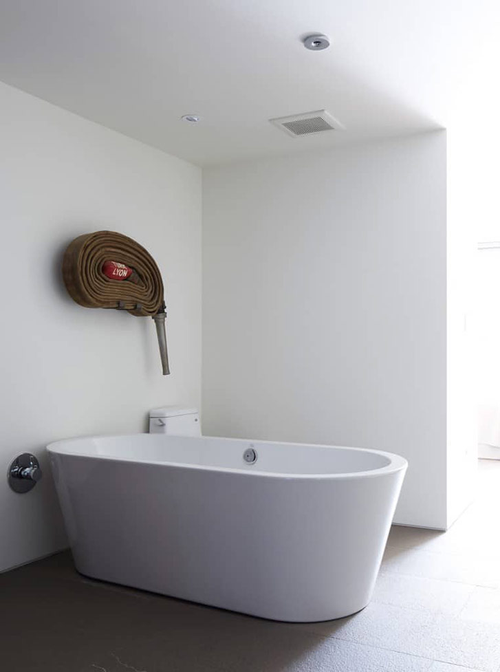 The floating Agape bathtub is filled by a Kohler ceiling spout, but guests often think the hose, a Graham Gillmore artwork mounted in the bathroom, is some arcane method for filling the basin.