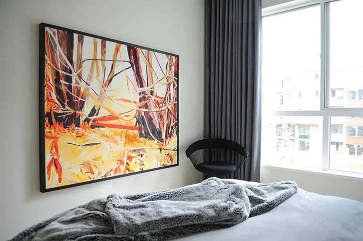 In the bedroom, a vibrant painting by Rob Nicholls adds a punch of warmth to the grey-and-white space.