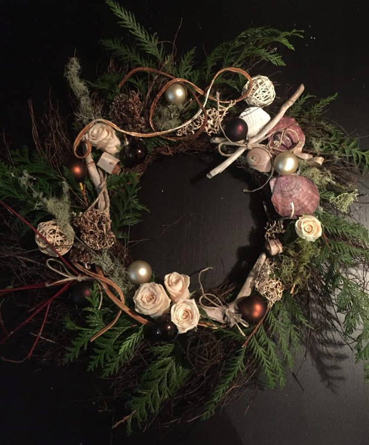 A festive holiday wreath with evergreen branches, flowers, and ornaments by Bespoke Blossoms.