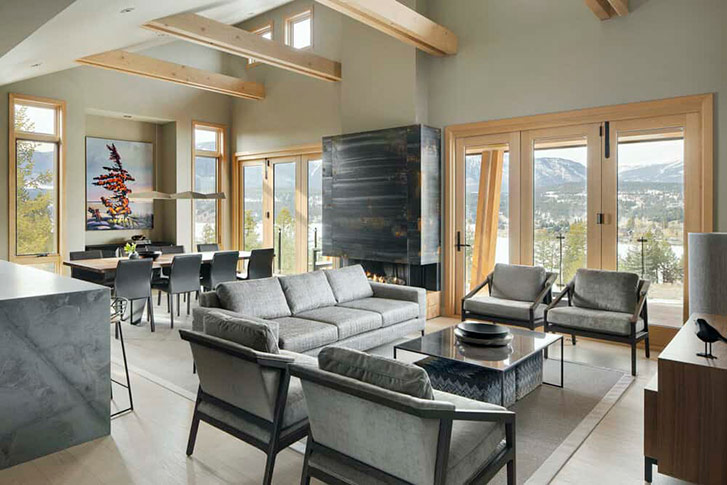 The living room of a mountain home. Bay windows overlook a scenic view of trees and lakefront.
