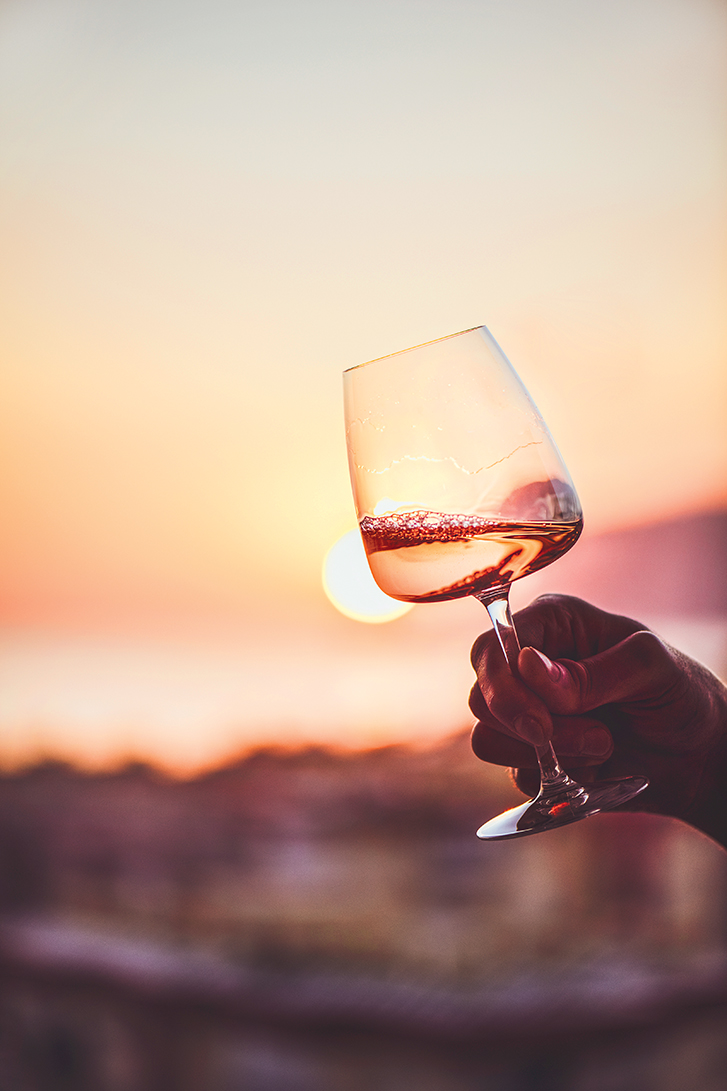 Glass of rose wine in mans hand with sea view and sunset